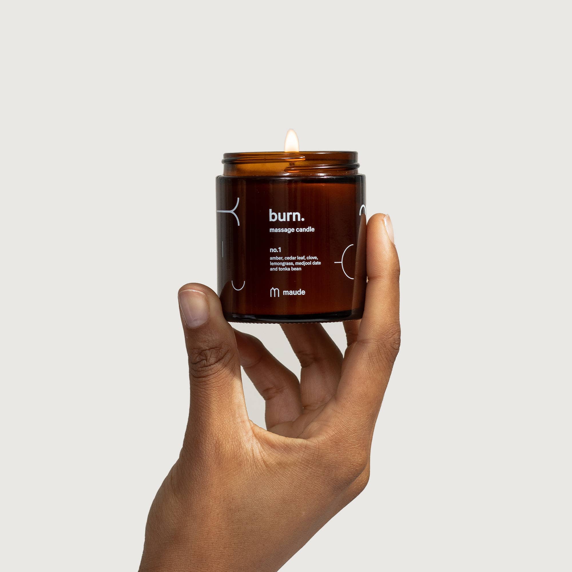 Hand holding a lit 'burn.' massage candle against a plain background