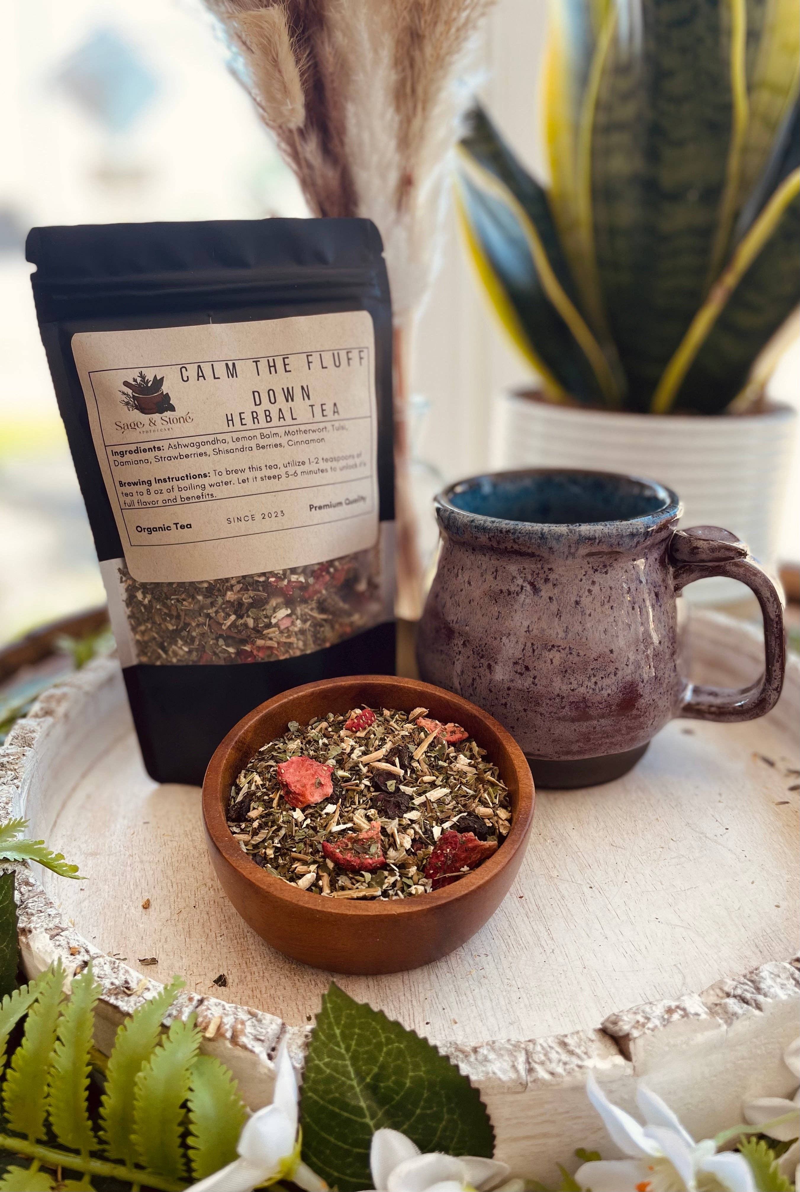 Tea packaging, mug, and bowl of tea leaves on a decorative surface with plants in the background.