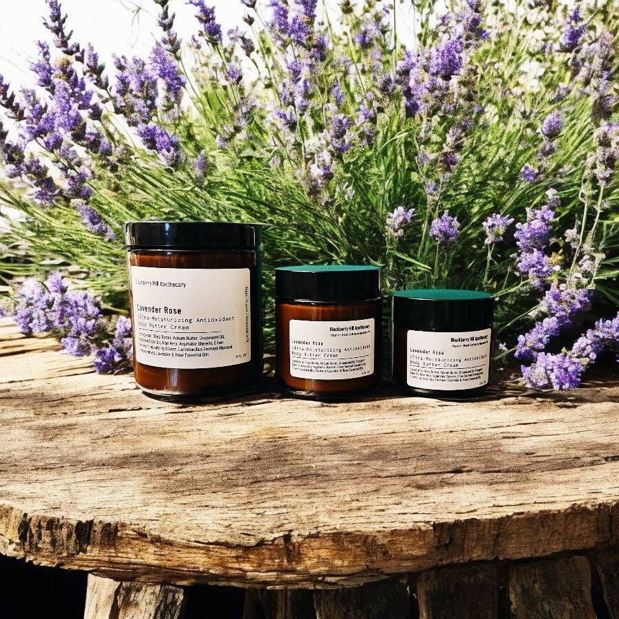 Three jars of body scrubs on a wooden surface with lavender flowers in the background