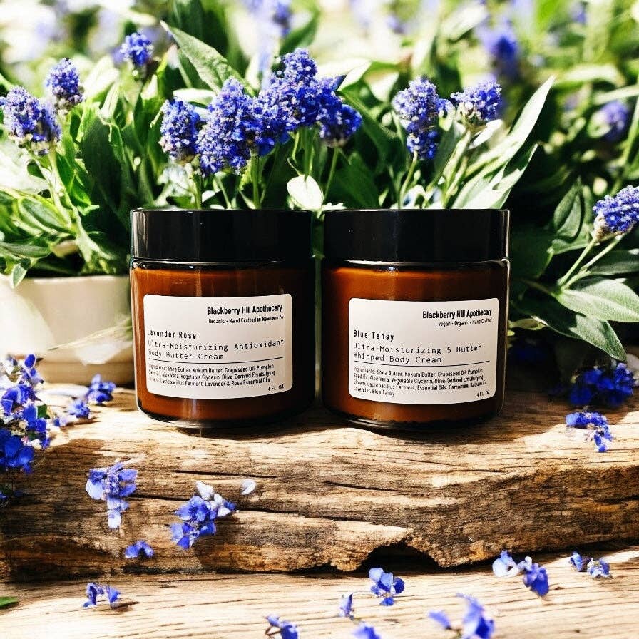 Two jars of body cream on a wooden surface with lavender flowers in the background