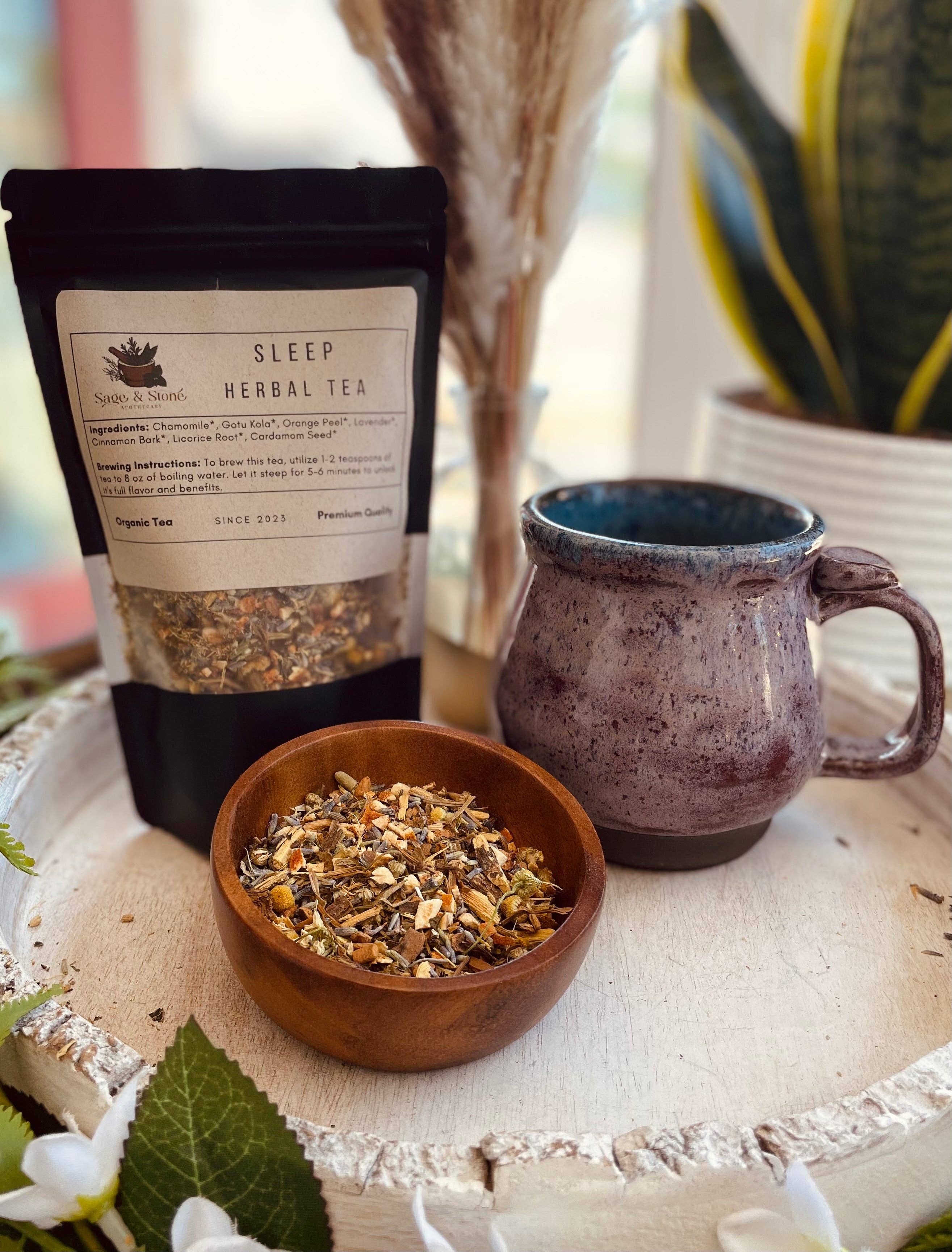 Sleep herbal tea package, wooden bowl with tea leaves, and ceramic mug on a textured surface.