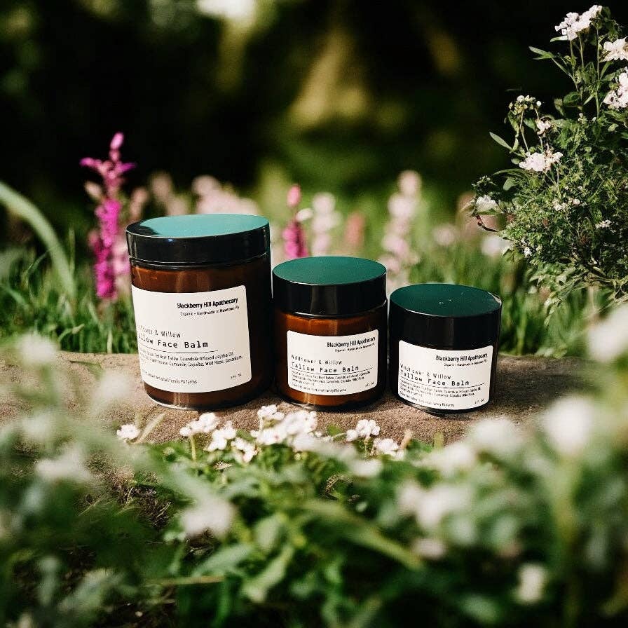 Three jars of Skindinavia face balm on a stone surface with a natural, blurred background of flowers and greenery.